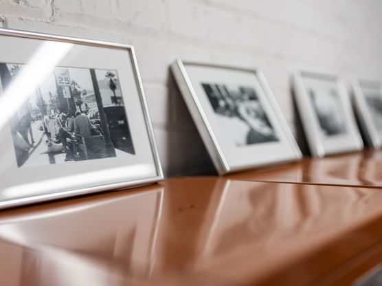 A series of black-and-white photographs in silver frames from a PNCA photography class sit on a wooden table