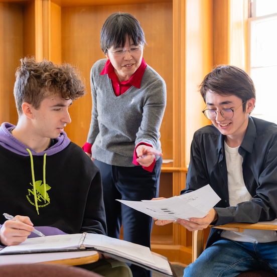 2 Willamette students work with a professor at their desks. 