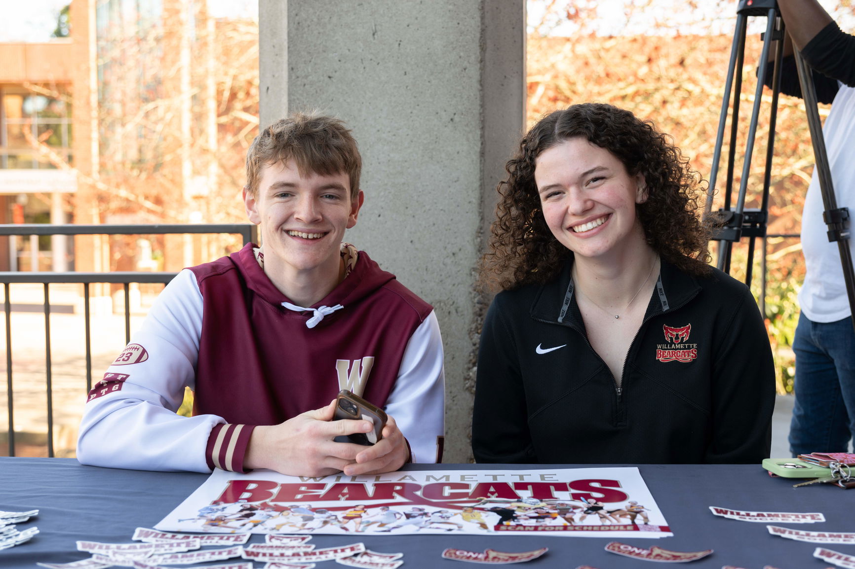 Two Willamette students sit at an informational table to welcome new students on Bearcat Day