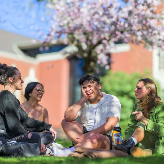 A group of laughing students sit together in the grass on Willamette's campus during Bearcat Day