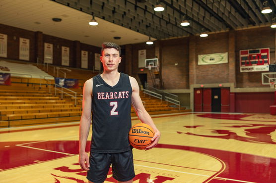 Willamette student Jack Boydell stands on a basketball court holding a basketball and wearing a Bearcats jerseyfpo