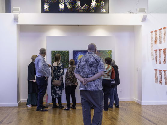 A group of people examine art on the wall of a PNCA gallery as part of an exhibition during commencement