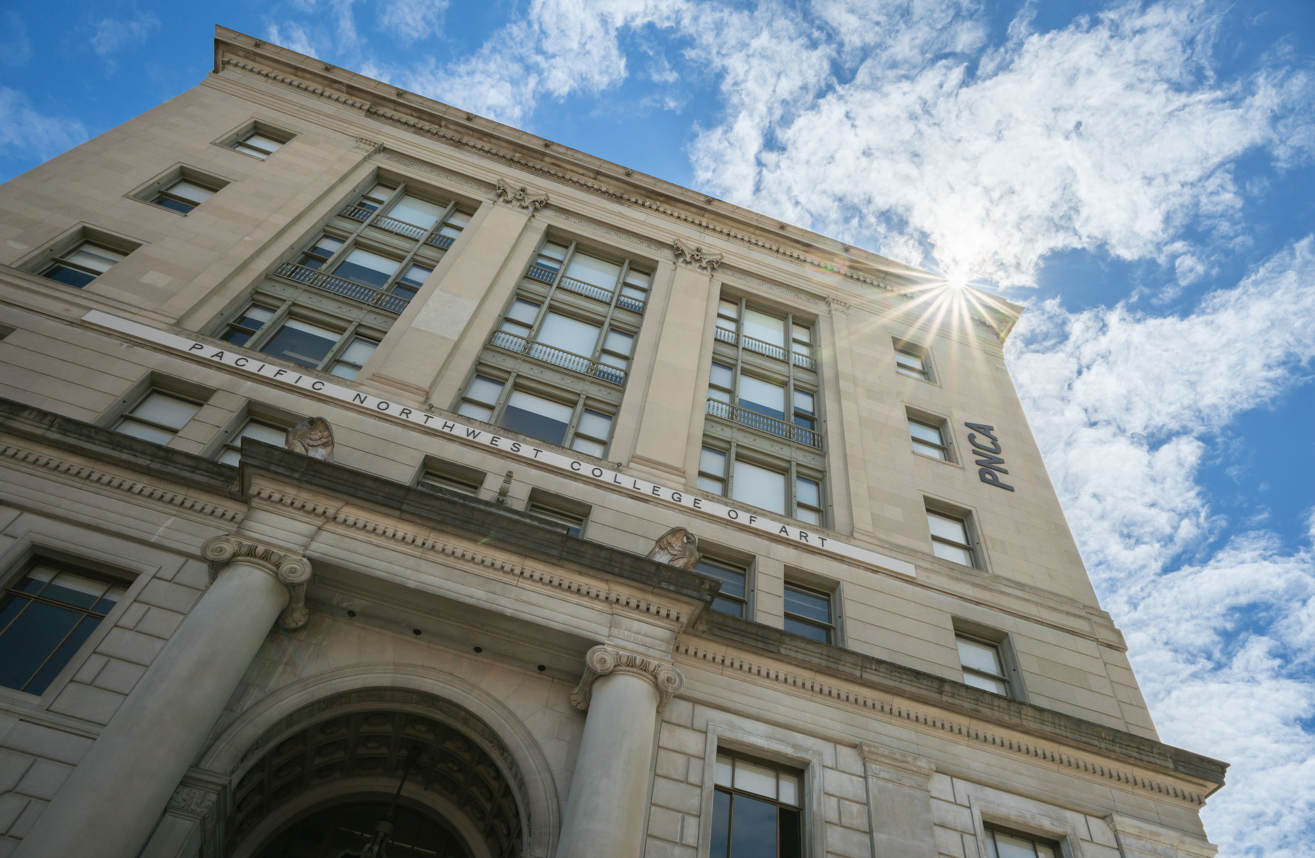 The exterior of PNCA as seen from below on a sunny day, a tall stone building with large windows