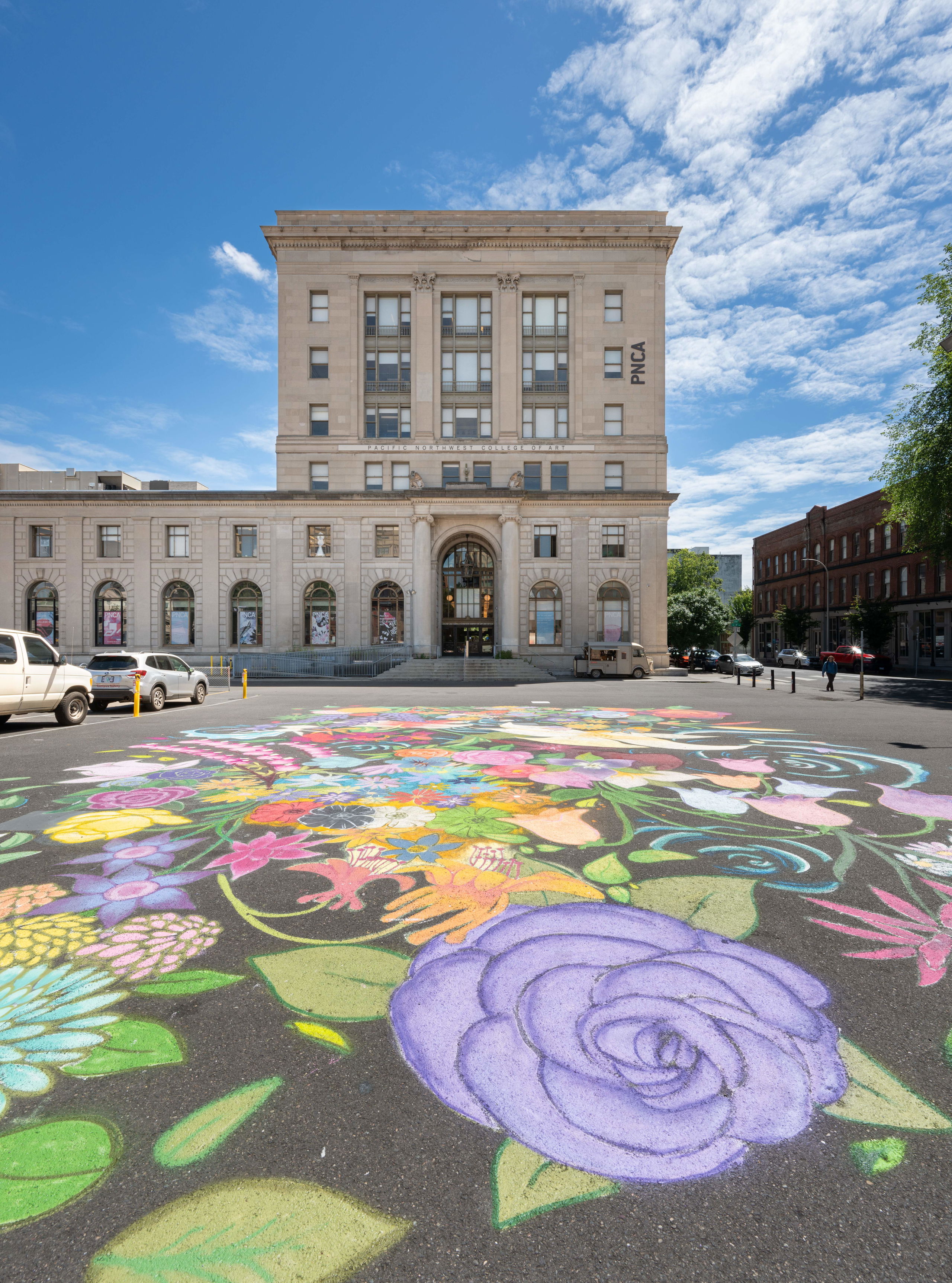 An asphalt street covered in chalk art of flowers in front of the white building that houses PNCA