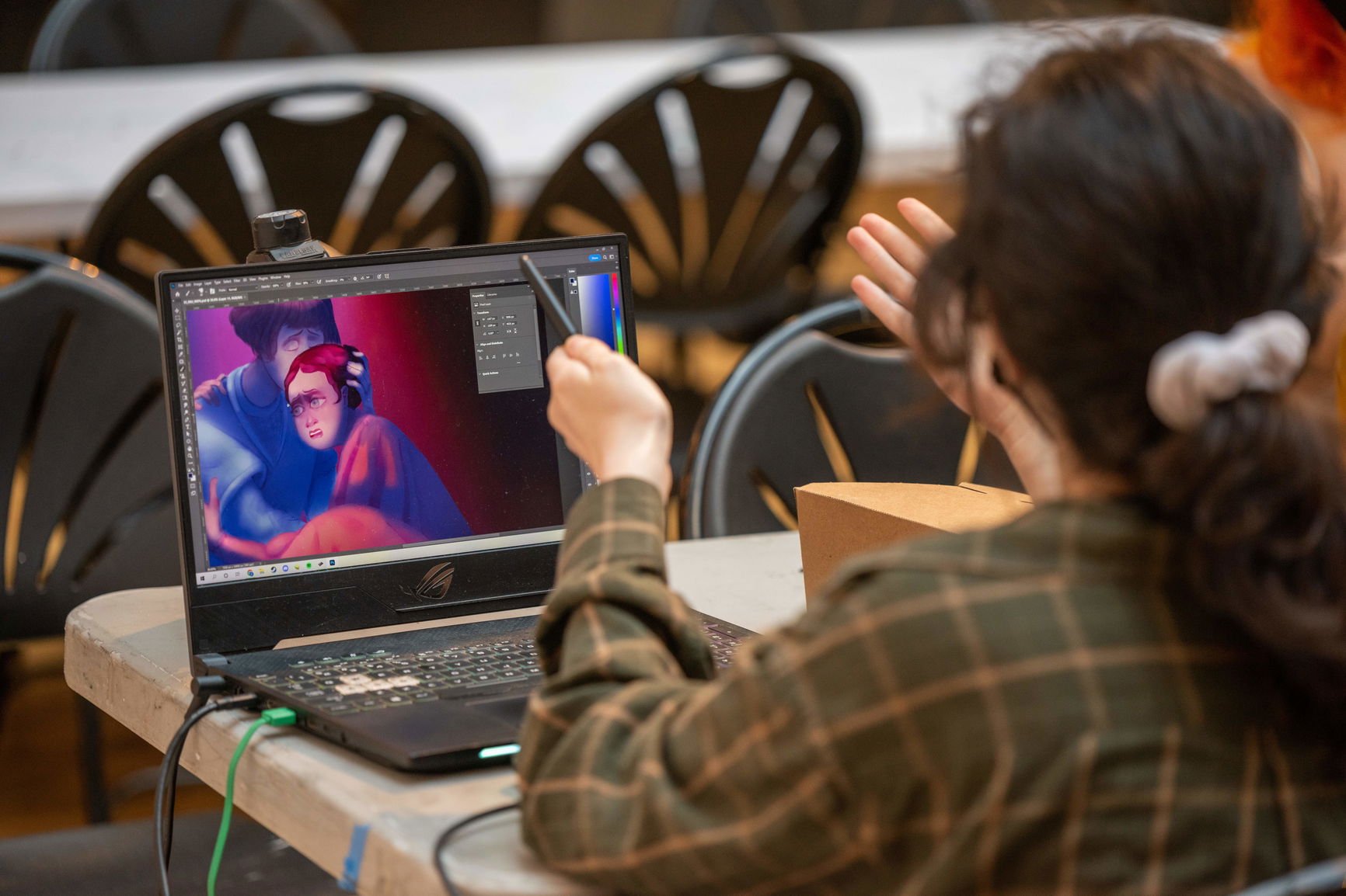 A PNCA student works on their laptop on a colorful illustration of two people embracing