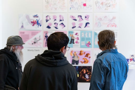 Three men examine a wall of graphic design art during a PNCA First Thursday event