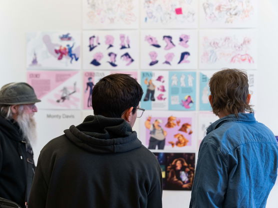 Three men examine a wall of graphic design art during a PNCA First Thursday event