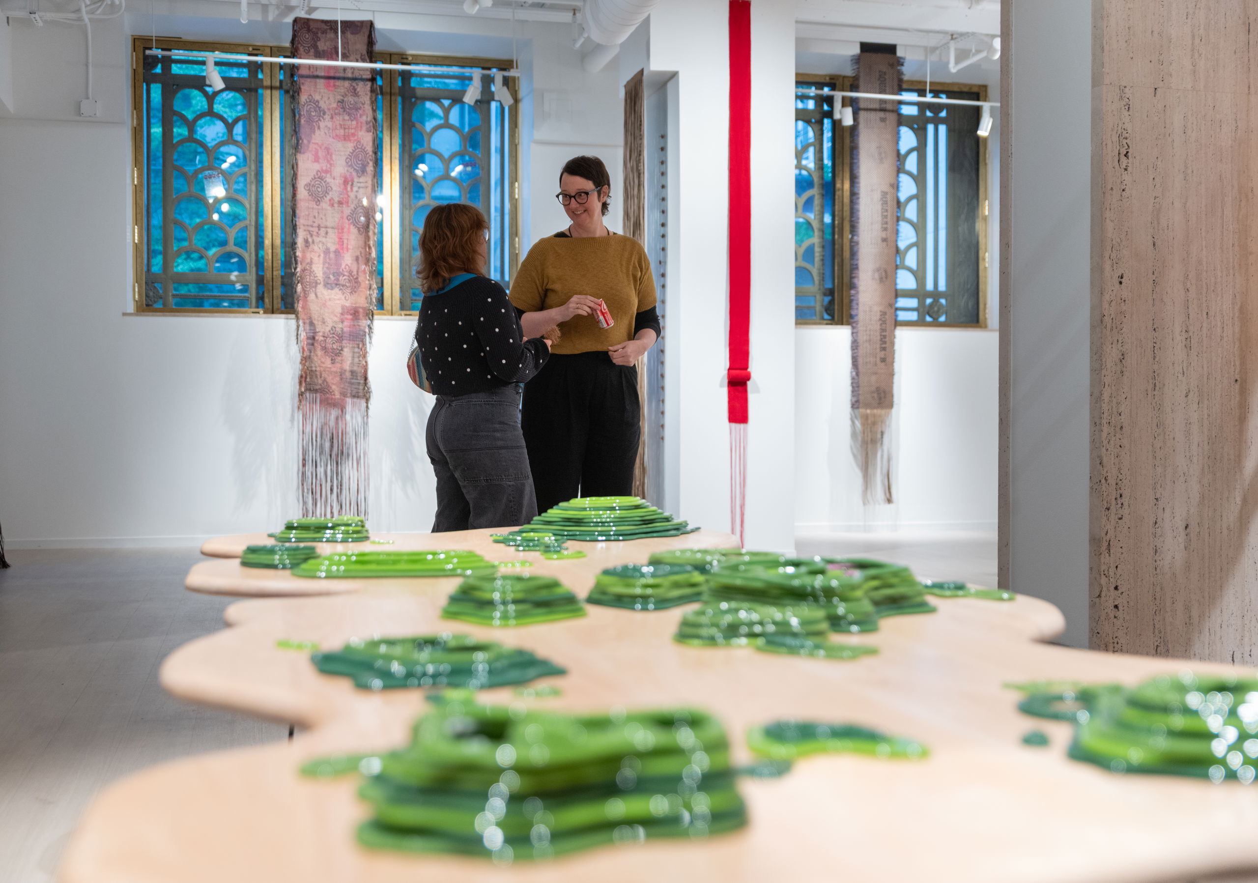 Two women stand chatting in front of a table covered in stacks of green plastic toys