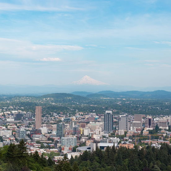 An aerial view of Portland, Oregon, a city surrounded by green rolling hills with a mountain in the distance