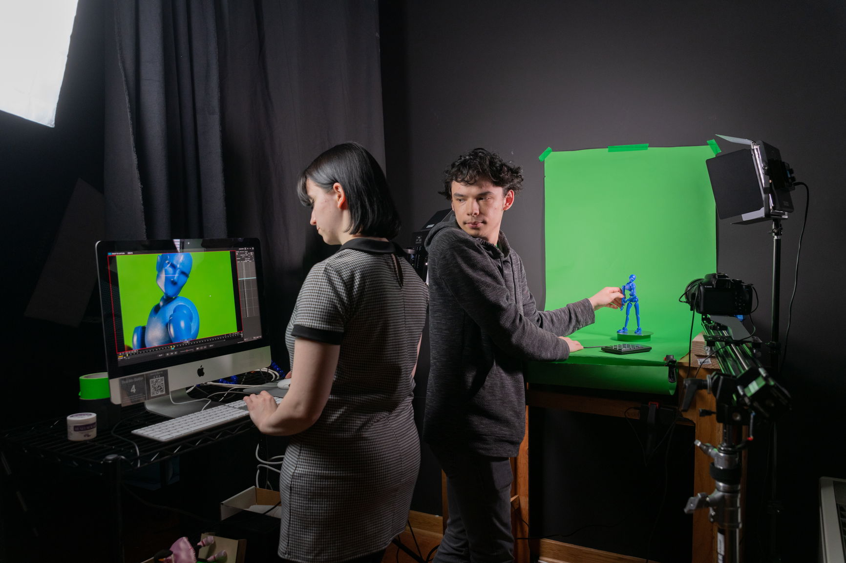 Two students working on an animation project using technology and a green screen