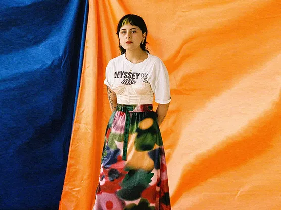 A woman standing in front of a yellow and blue backdrop wearing a white shirt and floral skirt