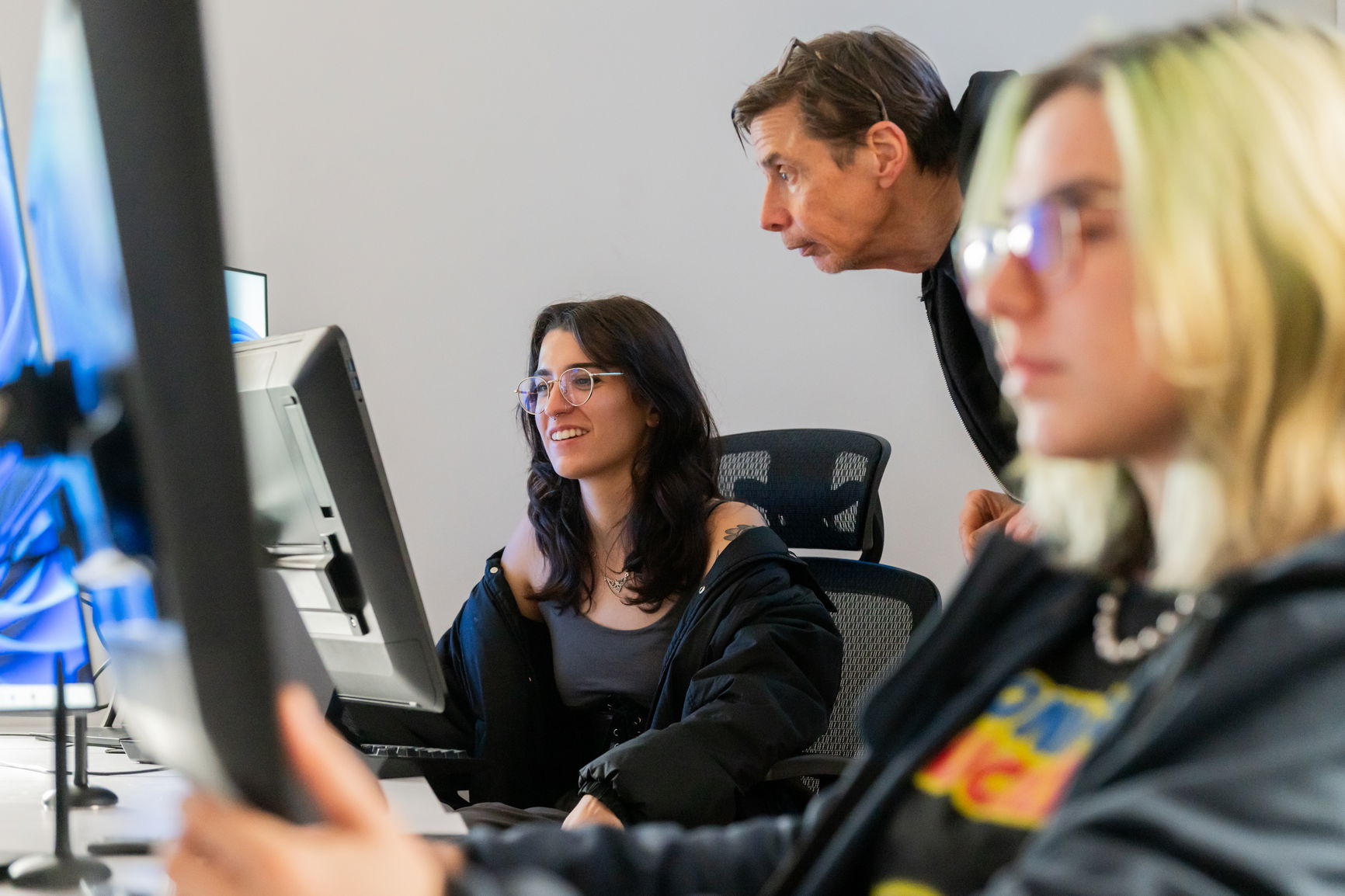 Two students working on a computer with a professor guiding them