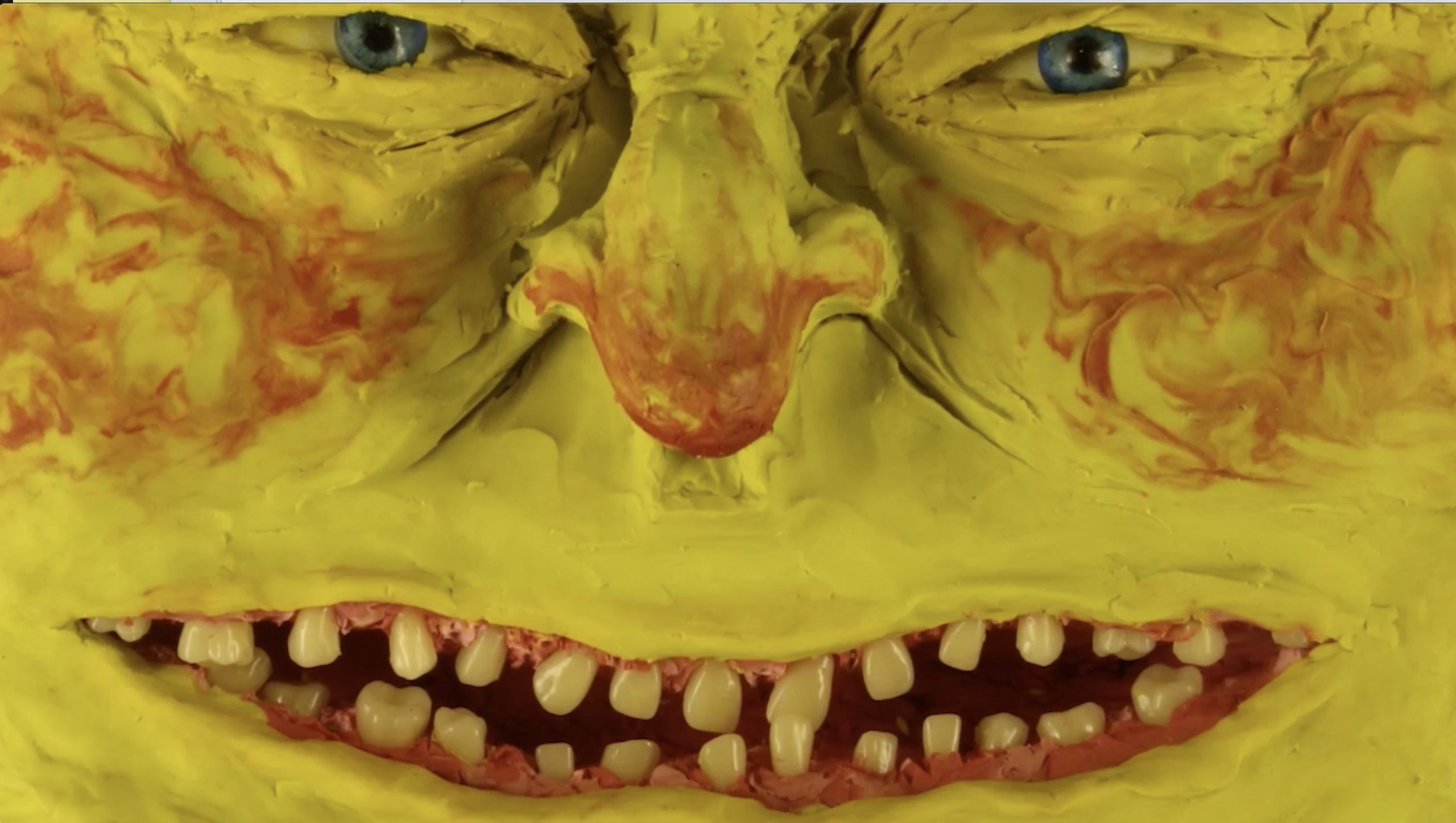 clay sculpture of a big yellow smirking face