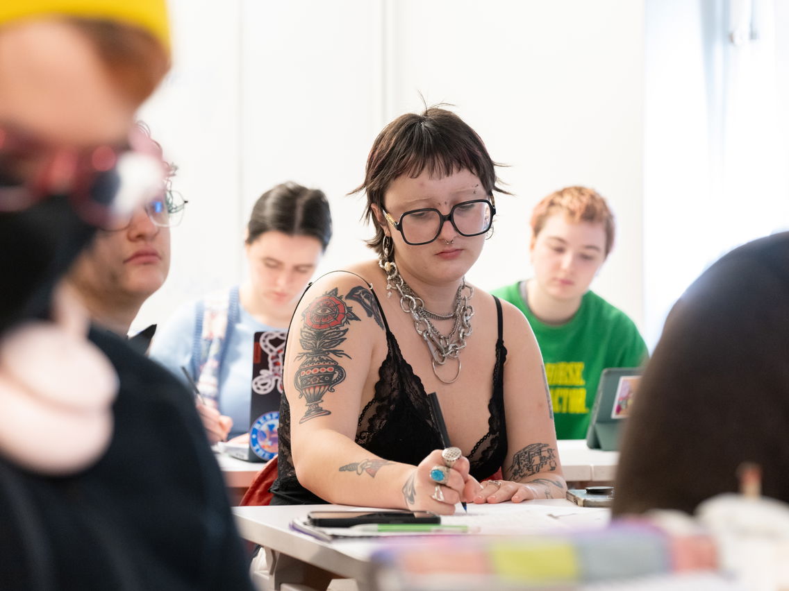 A student writing in a journal surrounded by other classmates