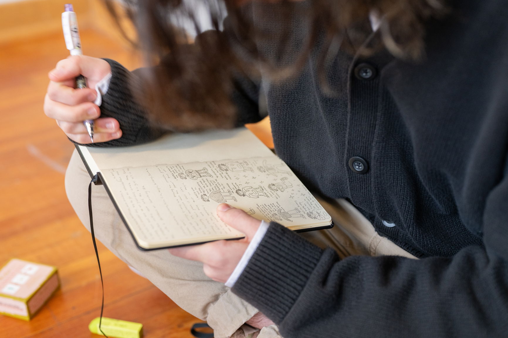 A person writing and creating sketches of people in a black notebook