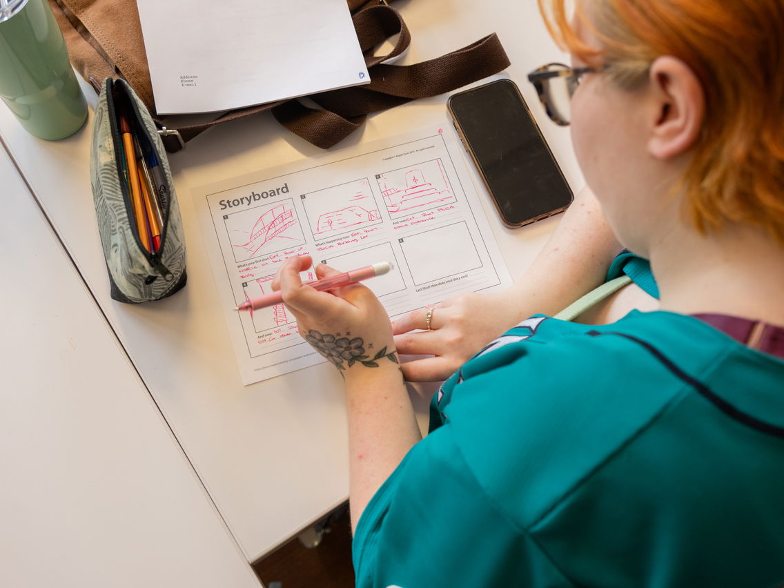 A student working through a storyboard project with a red pen