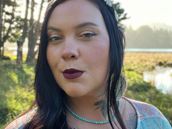 Close-up portrait of a person with long black hair wearing a decorative headband, turquoise bead necklace, and patterned top,