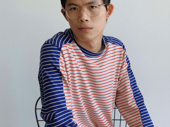 Young person wearing a gray cap, striped shirt, and rust-colored pants, sitting on a black wire chair.