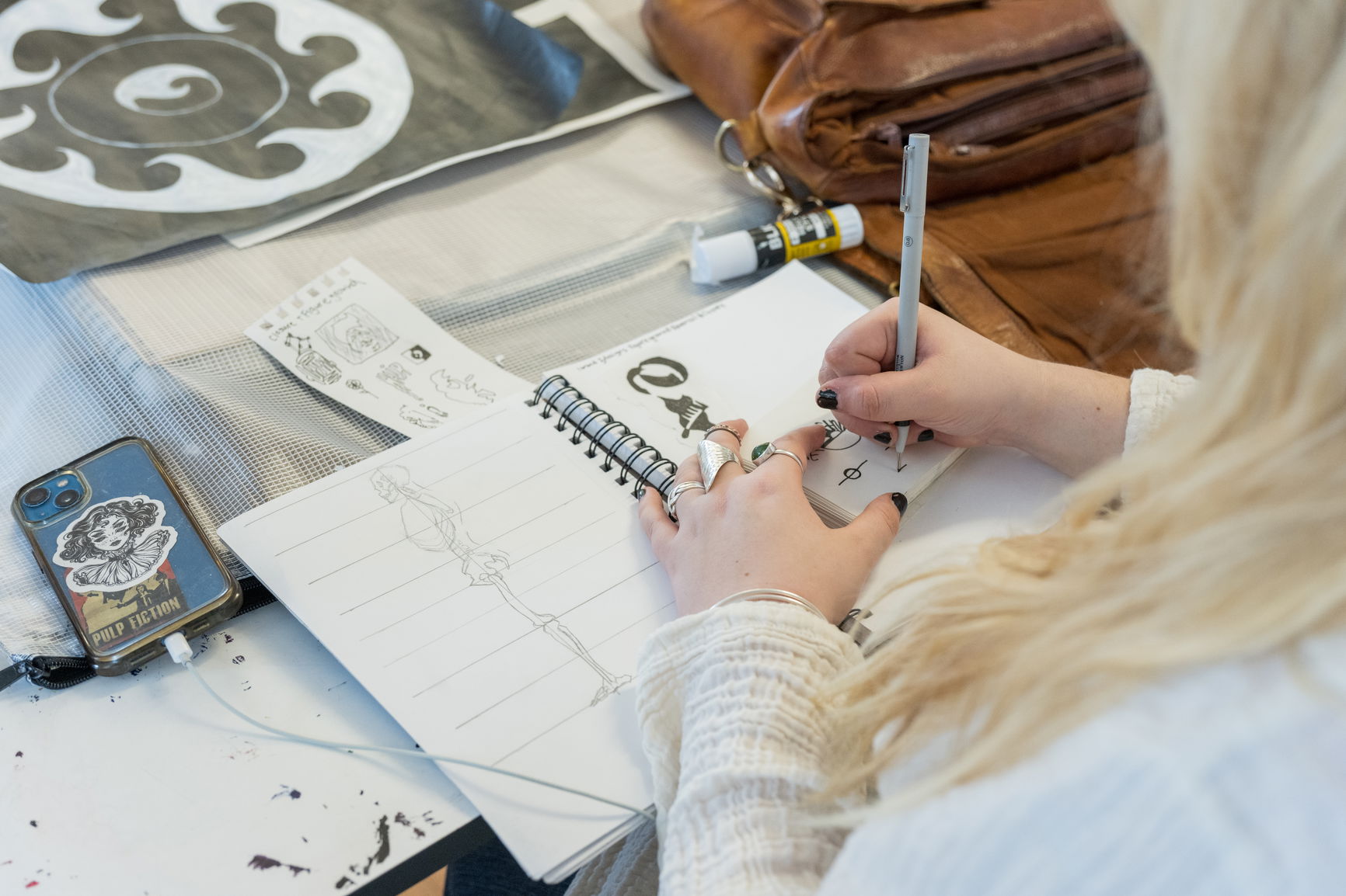 A person creating sketches with a pencile in a sketchbook while listening to music