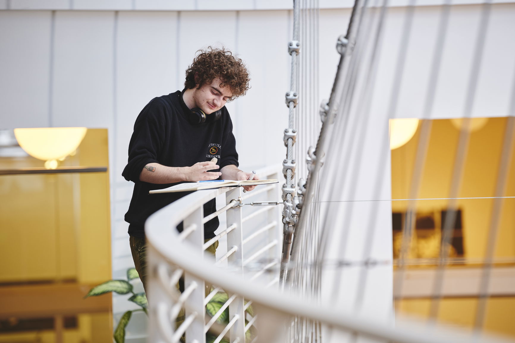 A young student standing on a staircase balcony working on an illustration