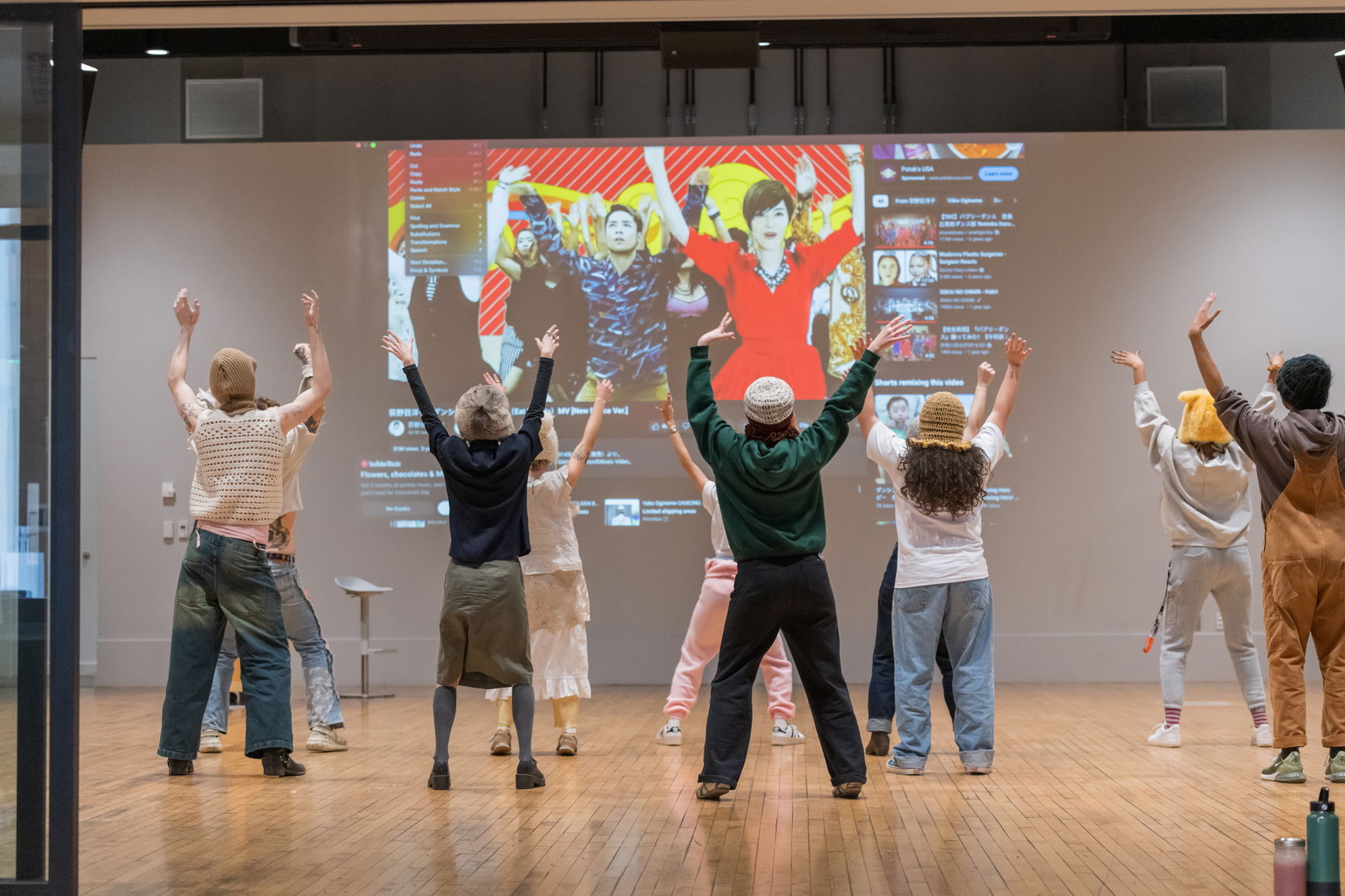 A group of people with their arms up in the sky facing a screen with other people with their hands up