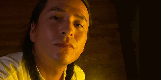 Close-up of a person with braided hair in a dimly lit room with a wooden panel background.