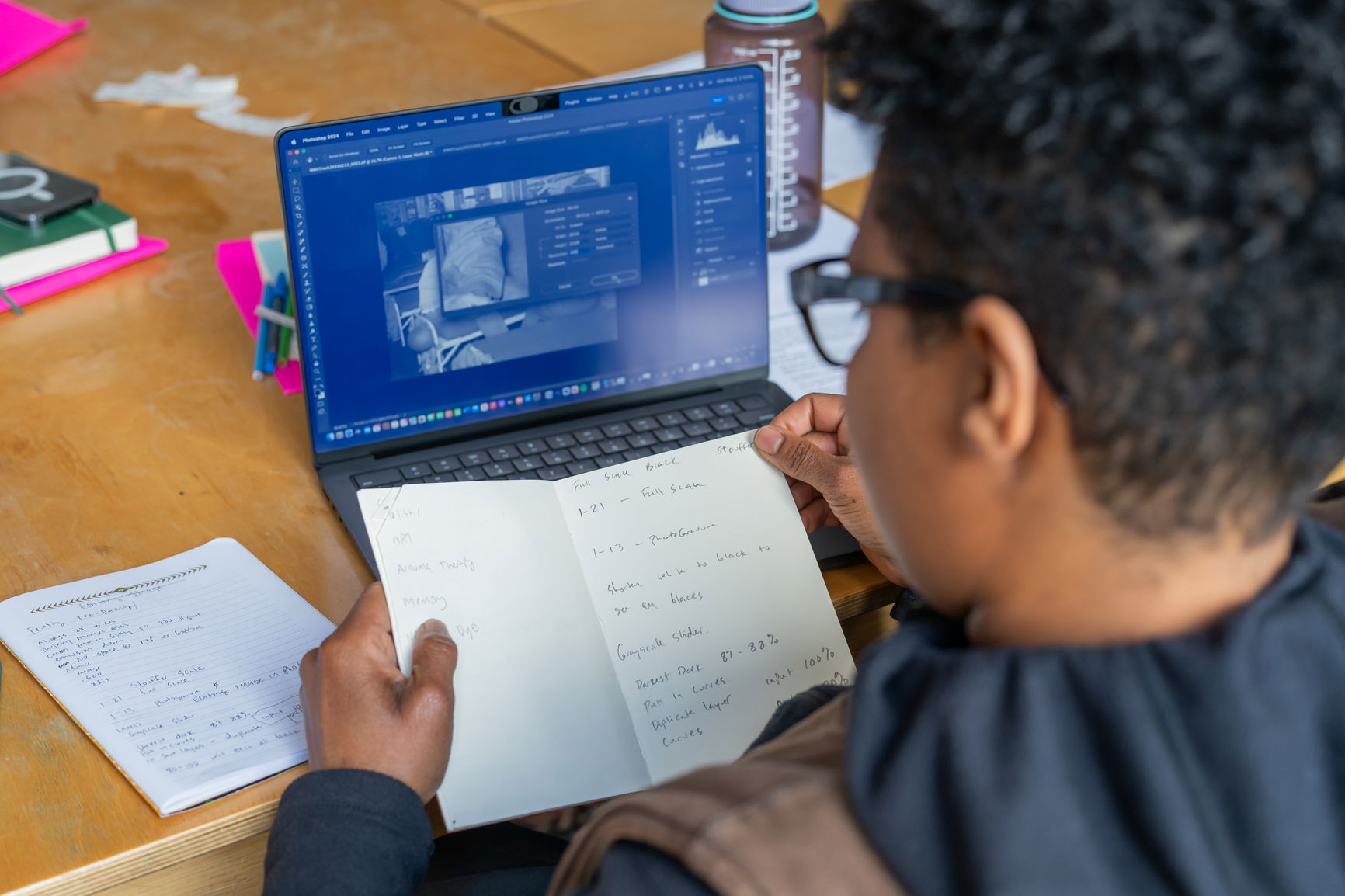 Person looking at a laptop while holding an open notebook with handwritten notes.