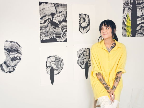 Woman in yellow shirt sitting in front of a wall adorned with abstract black and white art.