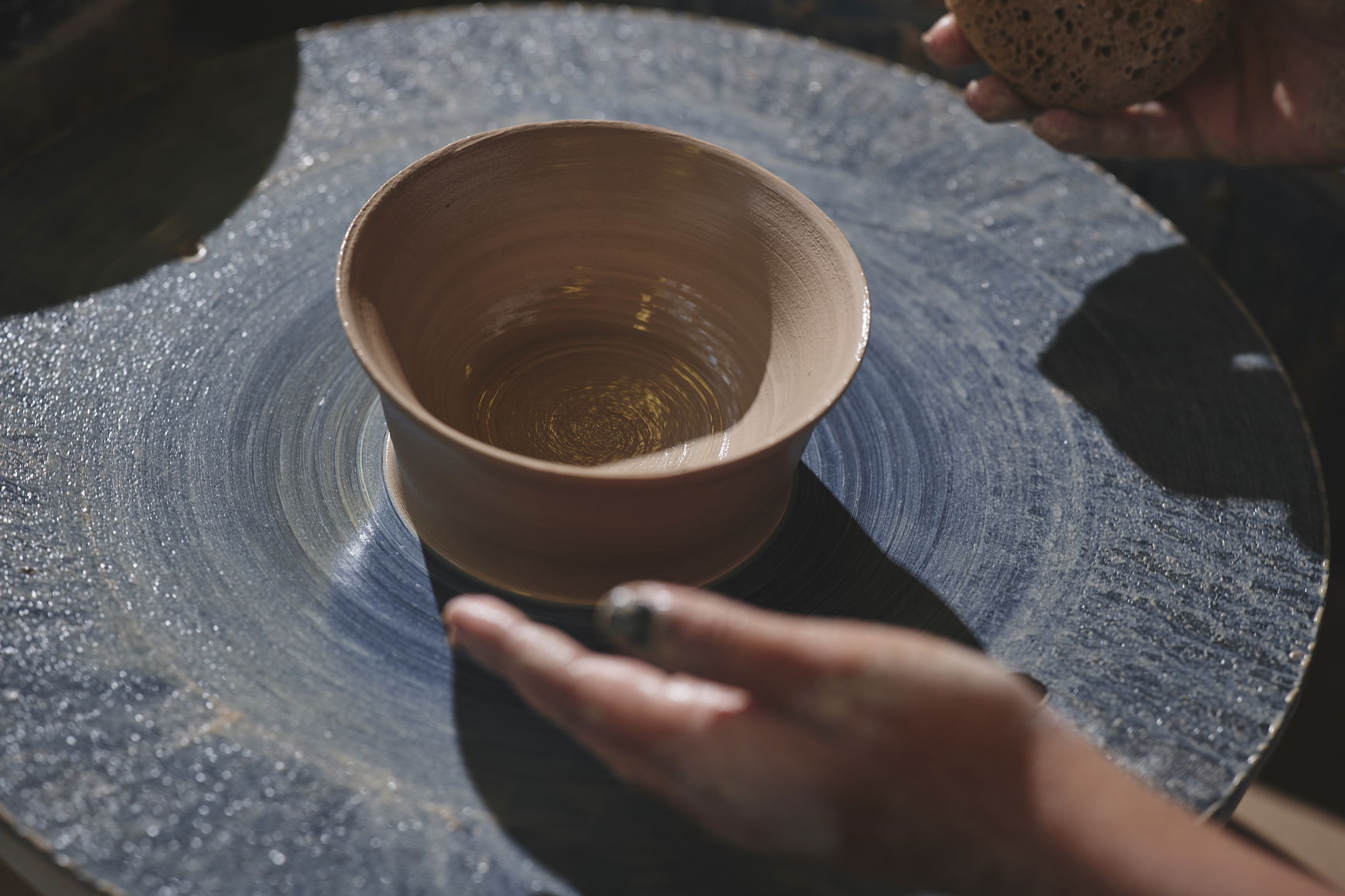 Hands shaping a clay bowl on a rotating pottery wheel.