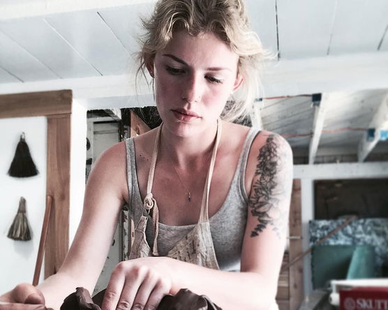 Person shaping clay inside a wooden bowl in a pottery studio.