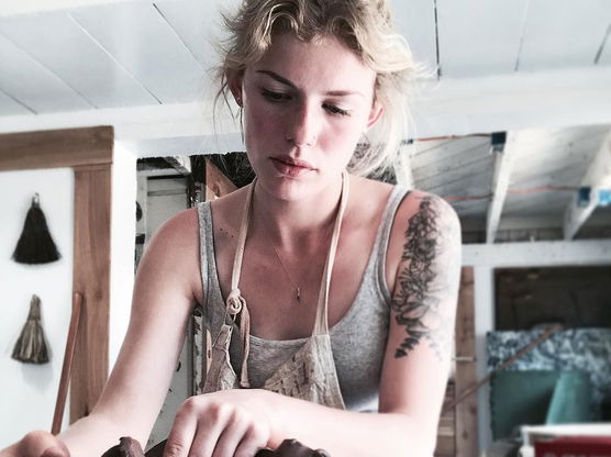 Person shaping clay inside a wooden bowl in a pottery studio.