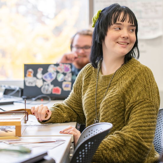 A student with black hair sitting at a desk and smiling.