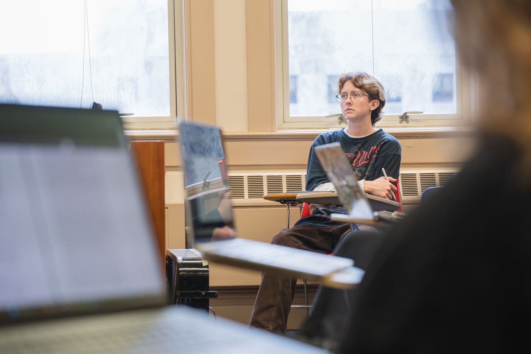 Student seated in a classroom, using a laptop and notebook.