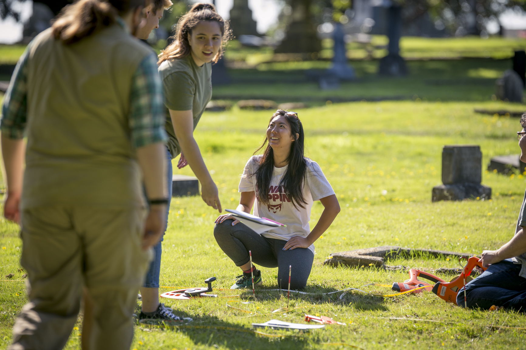 Two people in a grassy cemetery using a ground-penetrating radar device.