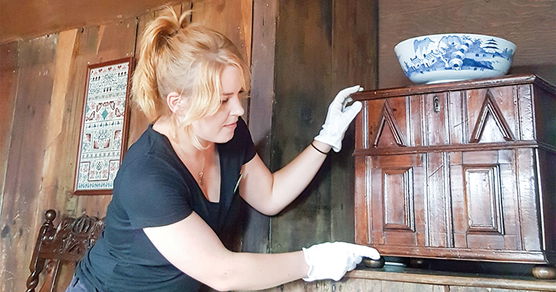 Woman in white gloves handling a small wooden cupboard with a blue and white bowl on top.