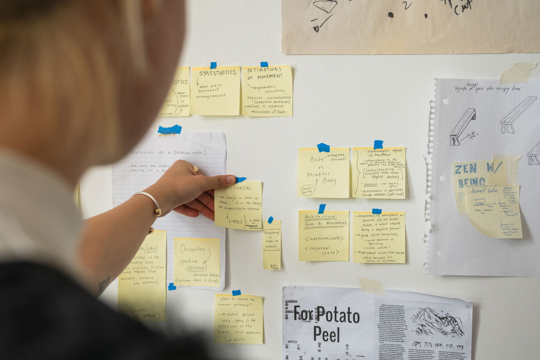 A person putting a sticky note on a wall with other yellow sticky notes