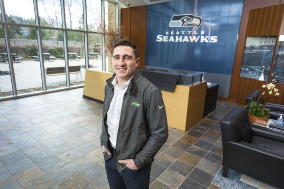 A man standing in a lobby with a Seattle Seahawks logo on the wall behind him.