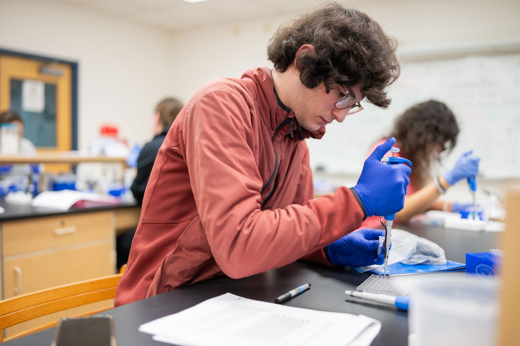 A student with glasses dropping liquid from a syringe into a test kit