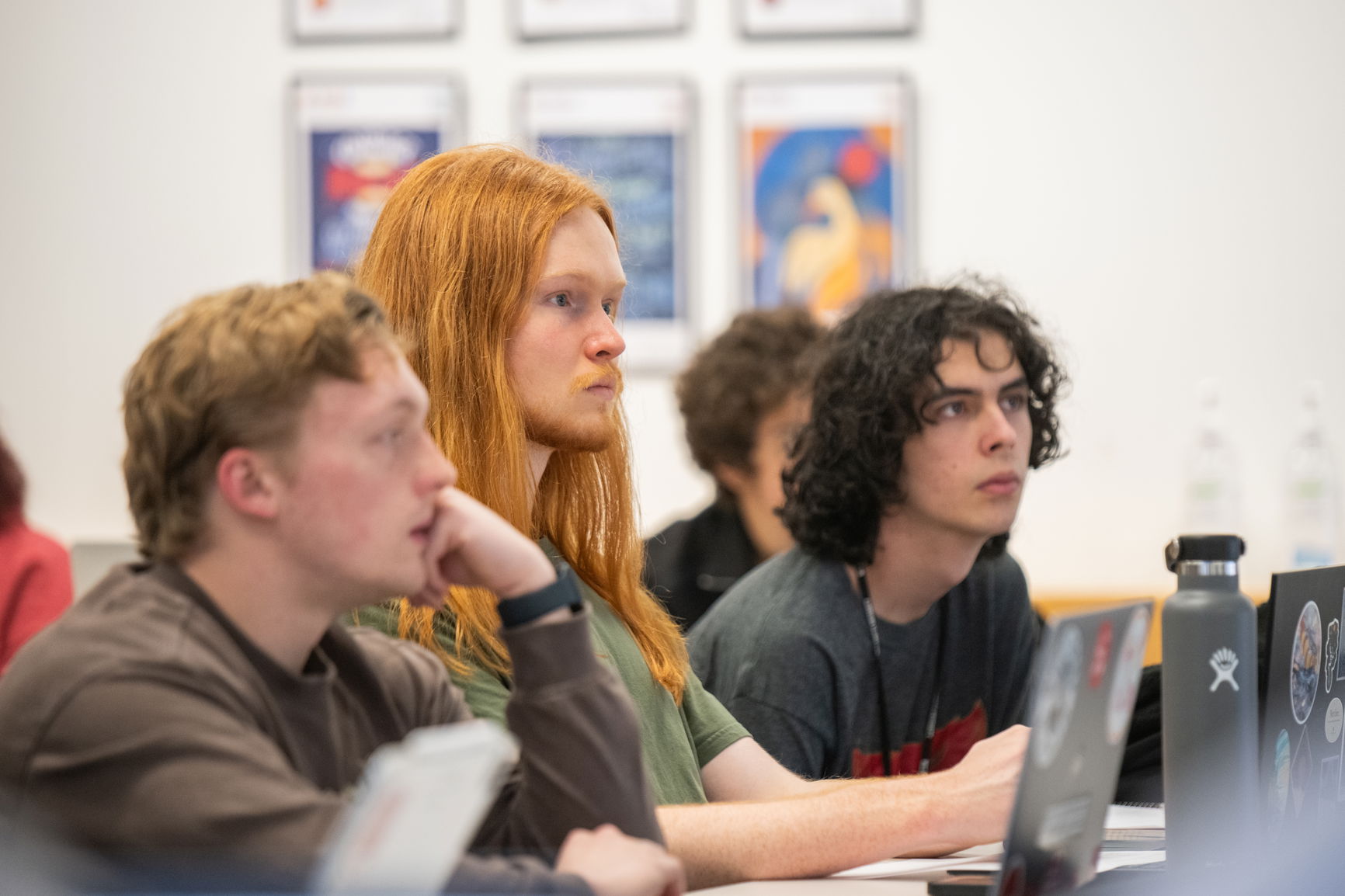 Three young men behind their laptops in a classroom setting