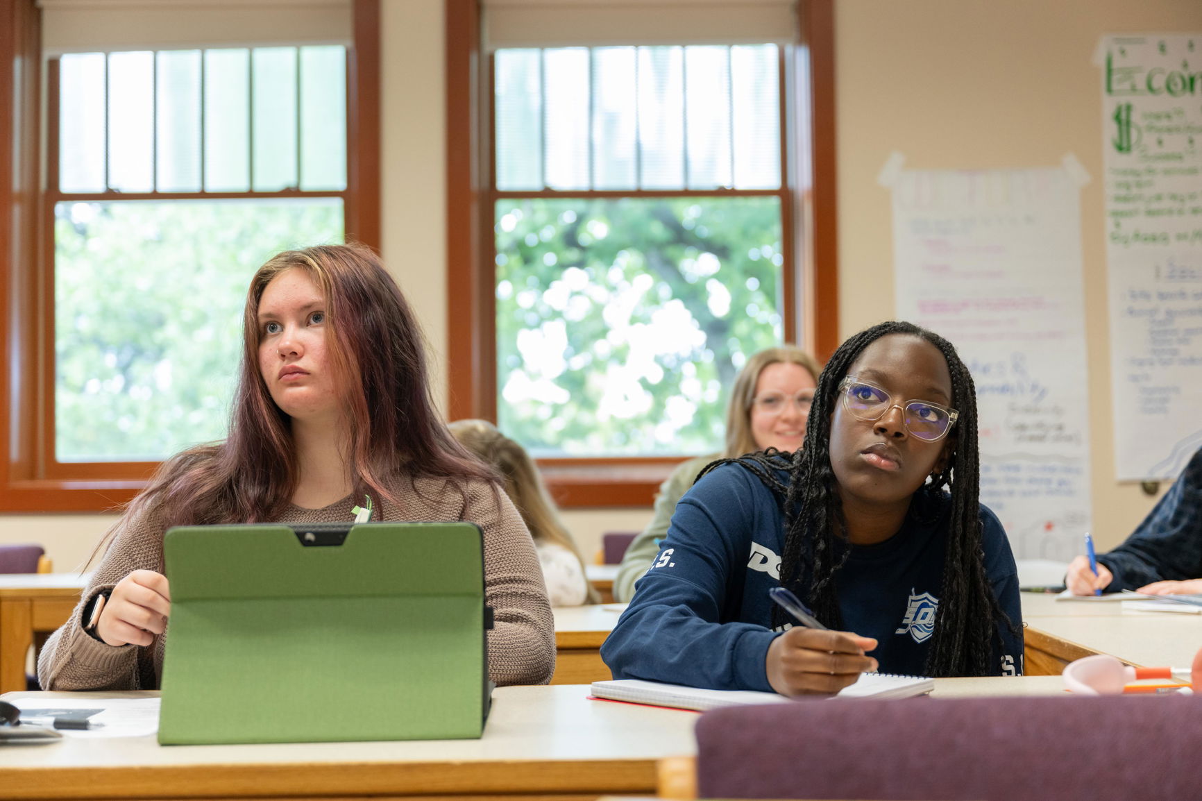 Two students sitting in the front of a class with their laptops looking up.