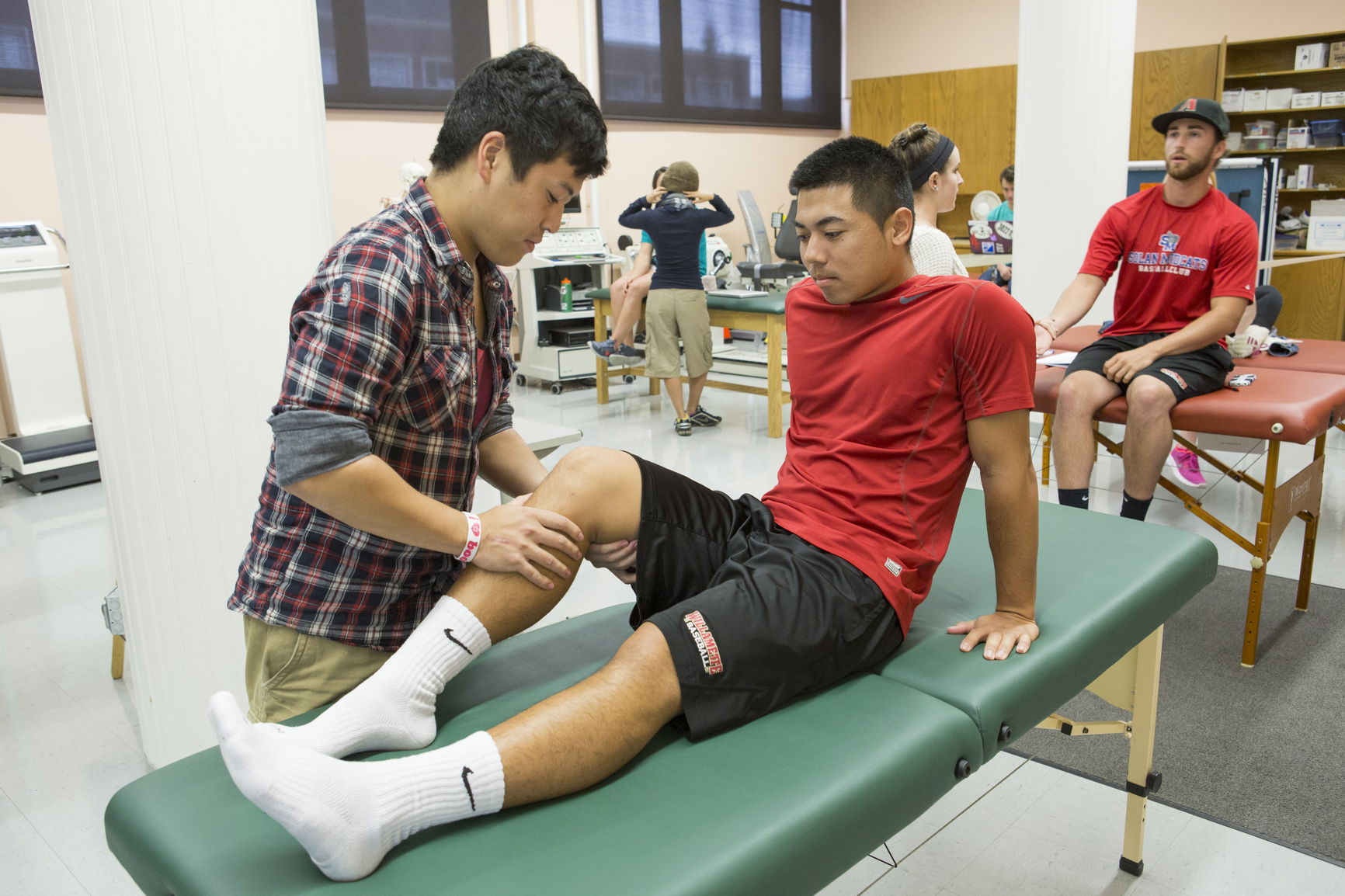 Therapist examines an athlete's knee on an examination table in a sports therapy facility.