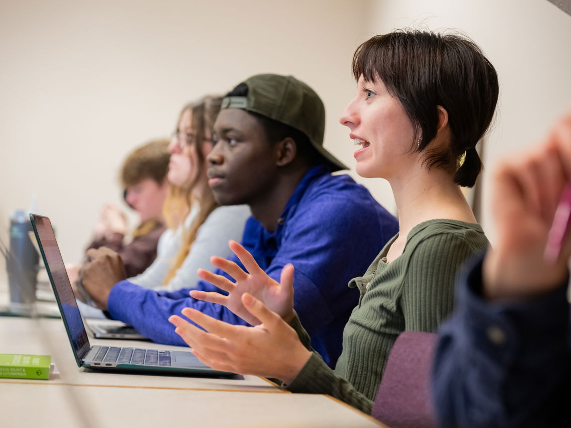 A student sitting alongside other classmates speaking towards the front of the room