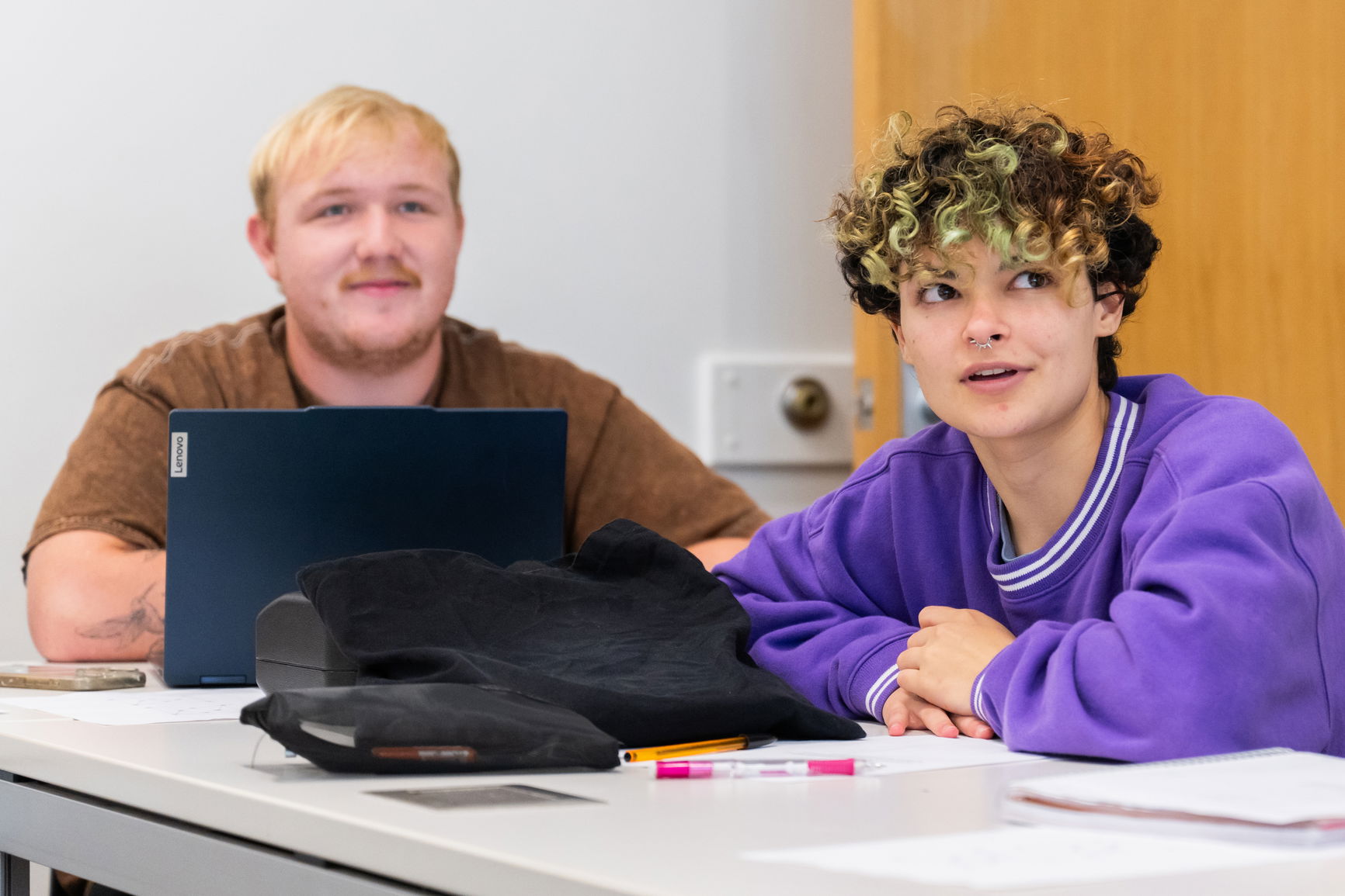 Two students working at a desk during a class. 