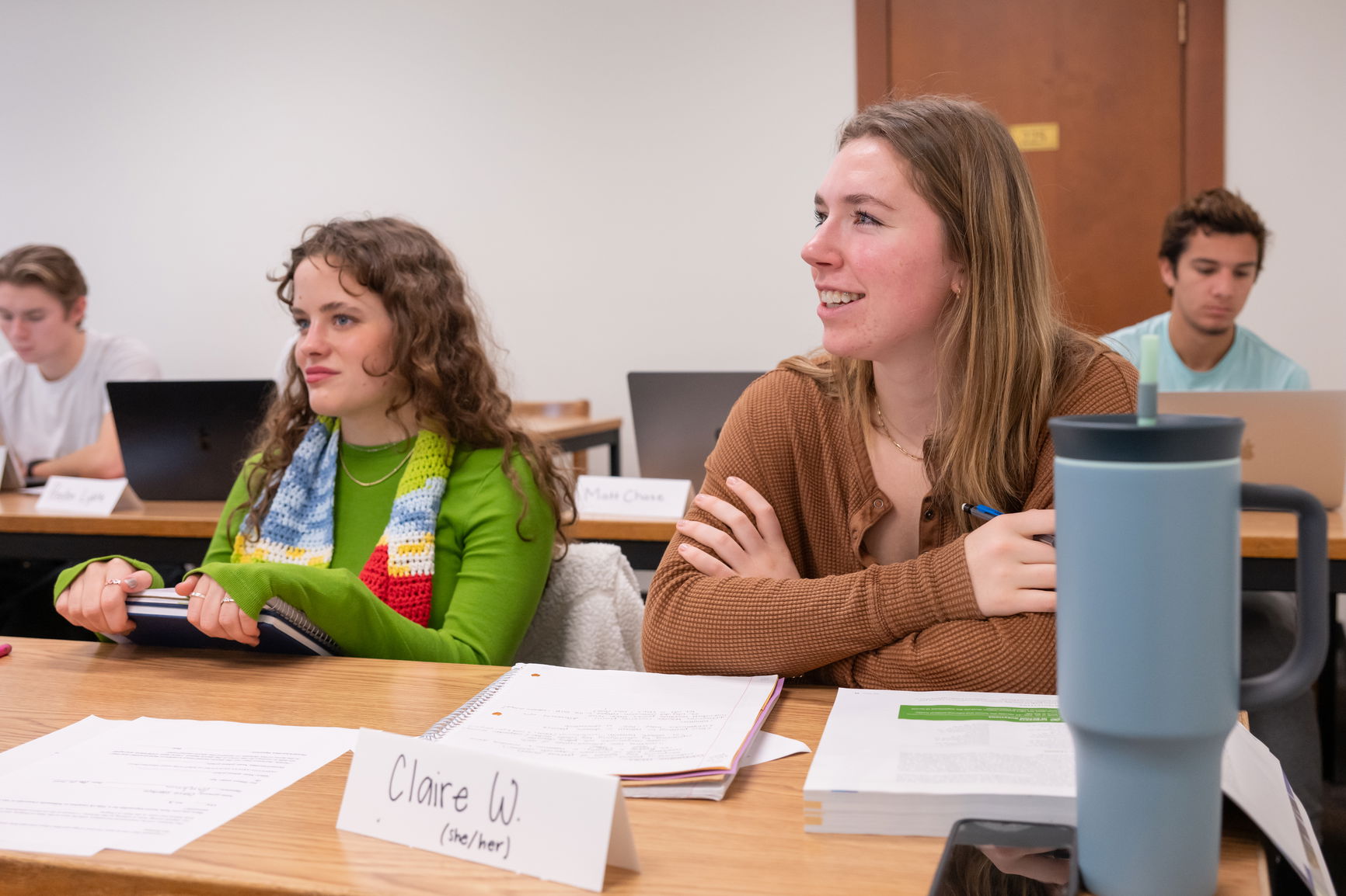 Students sitting at desks in a classroom, with name placards on their desks. The placard in the foreground reads 