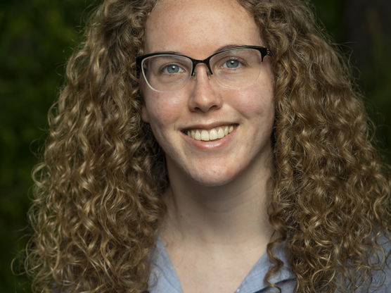 A curly haired blonde woman with black rimmed glasses and a blue shirt