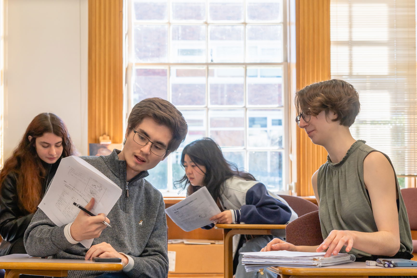 A group of students seated in desks reviewing a work paper