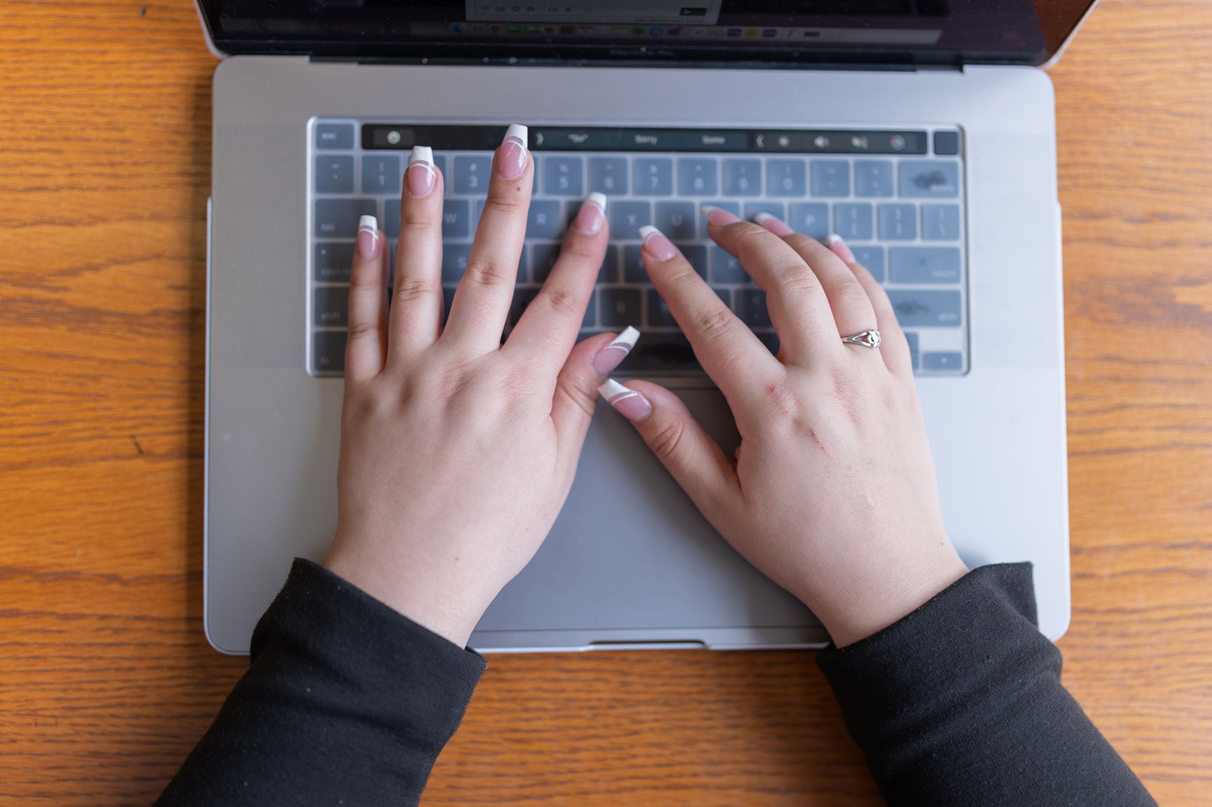 Hands with French manicure typing on a silver laptop.