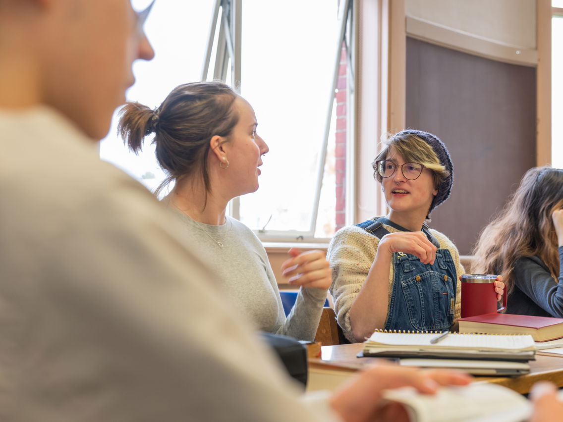 Group of people conversing around a table with books and notebooks.