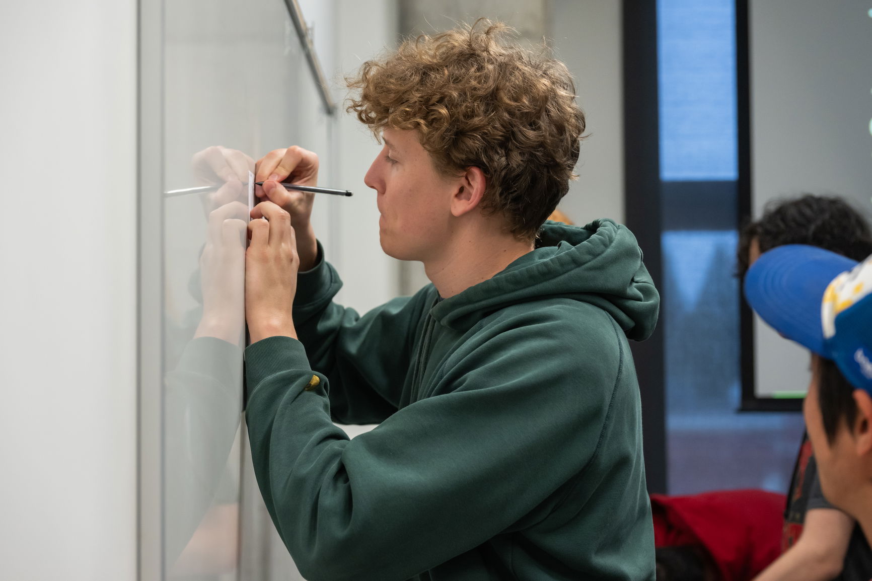 Person with curly hair writing on a whiteboard with a black marker.