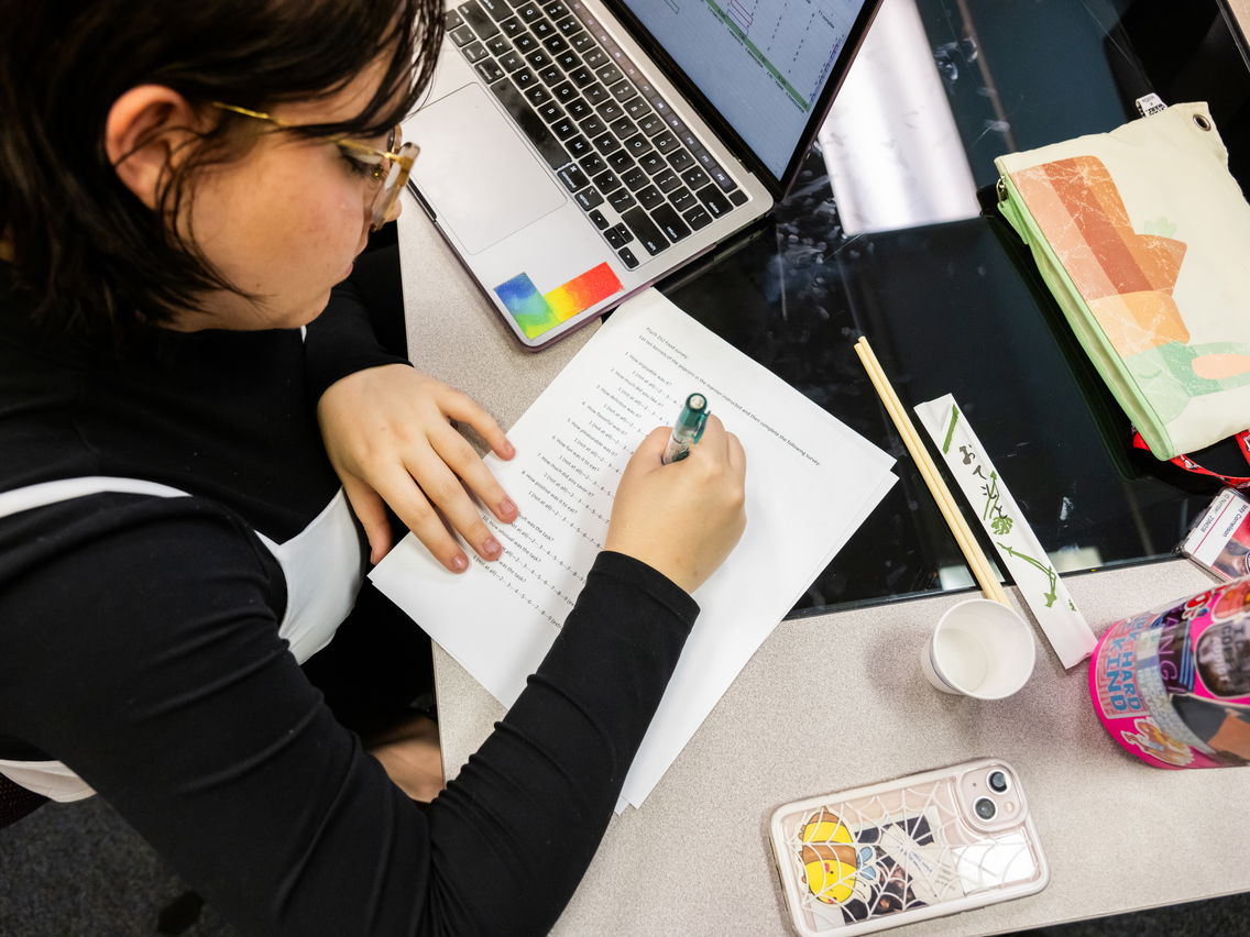 Student writing in a notebook with a laptop in the psych lab. 